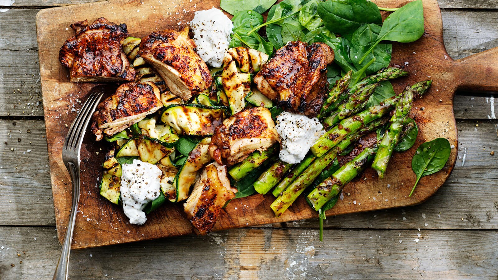 Grilled chicken and veggies plated on a wooden cutting board.