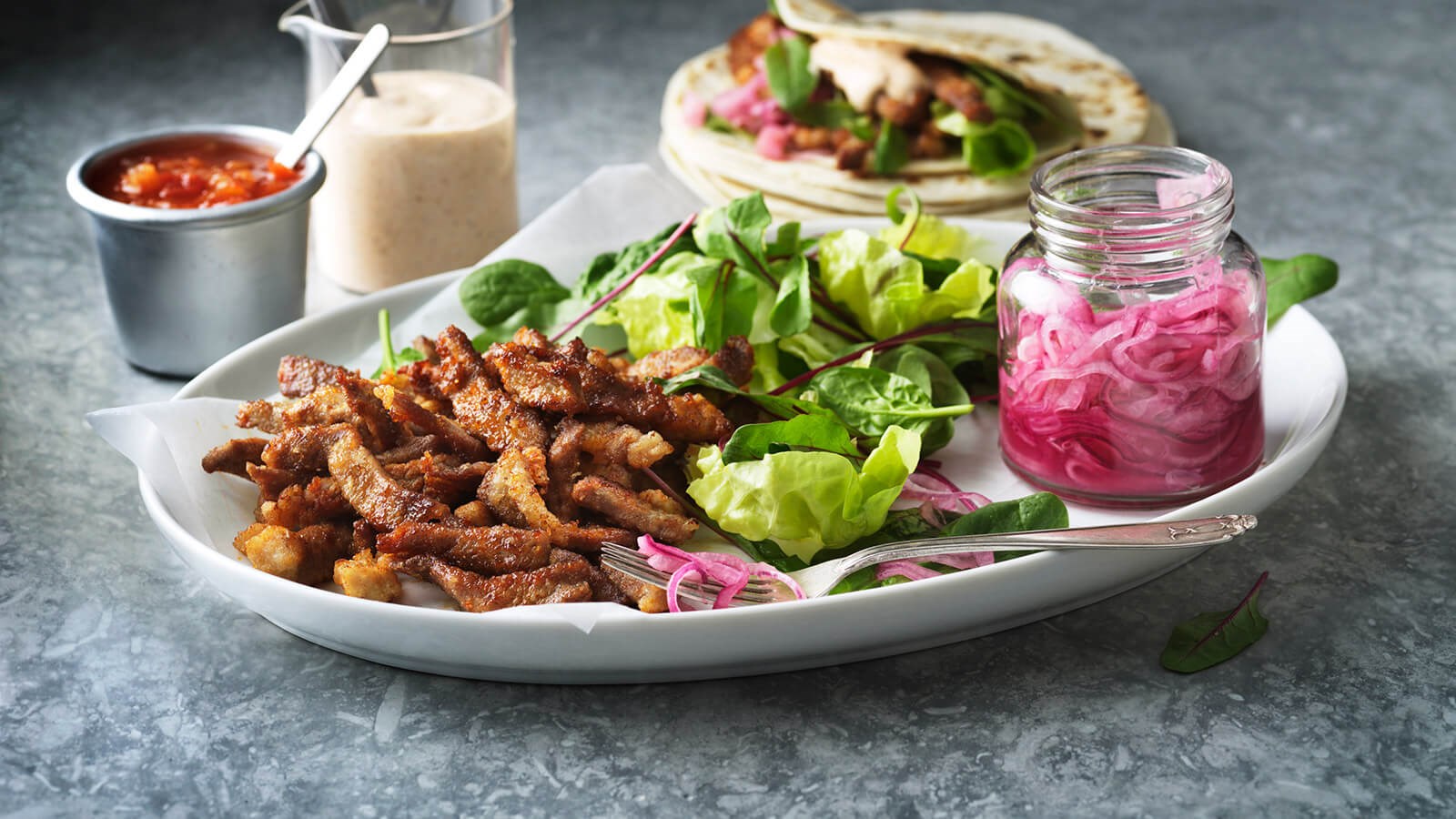 Chicharrónes on a plate with pickled red onions in a jar