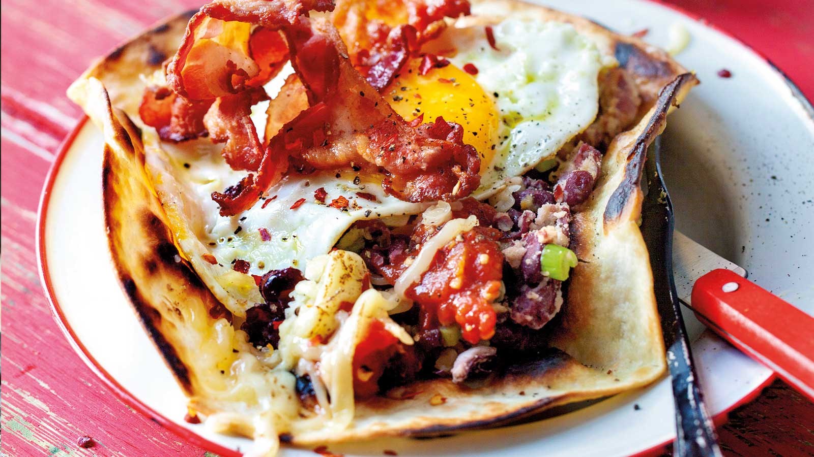 Open breakfast tortilla with fried eggs, grilled tomatoes, salsa and baked beans